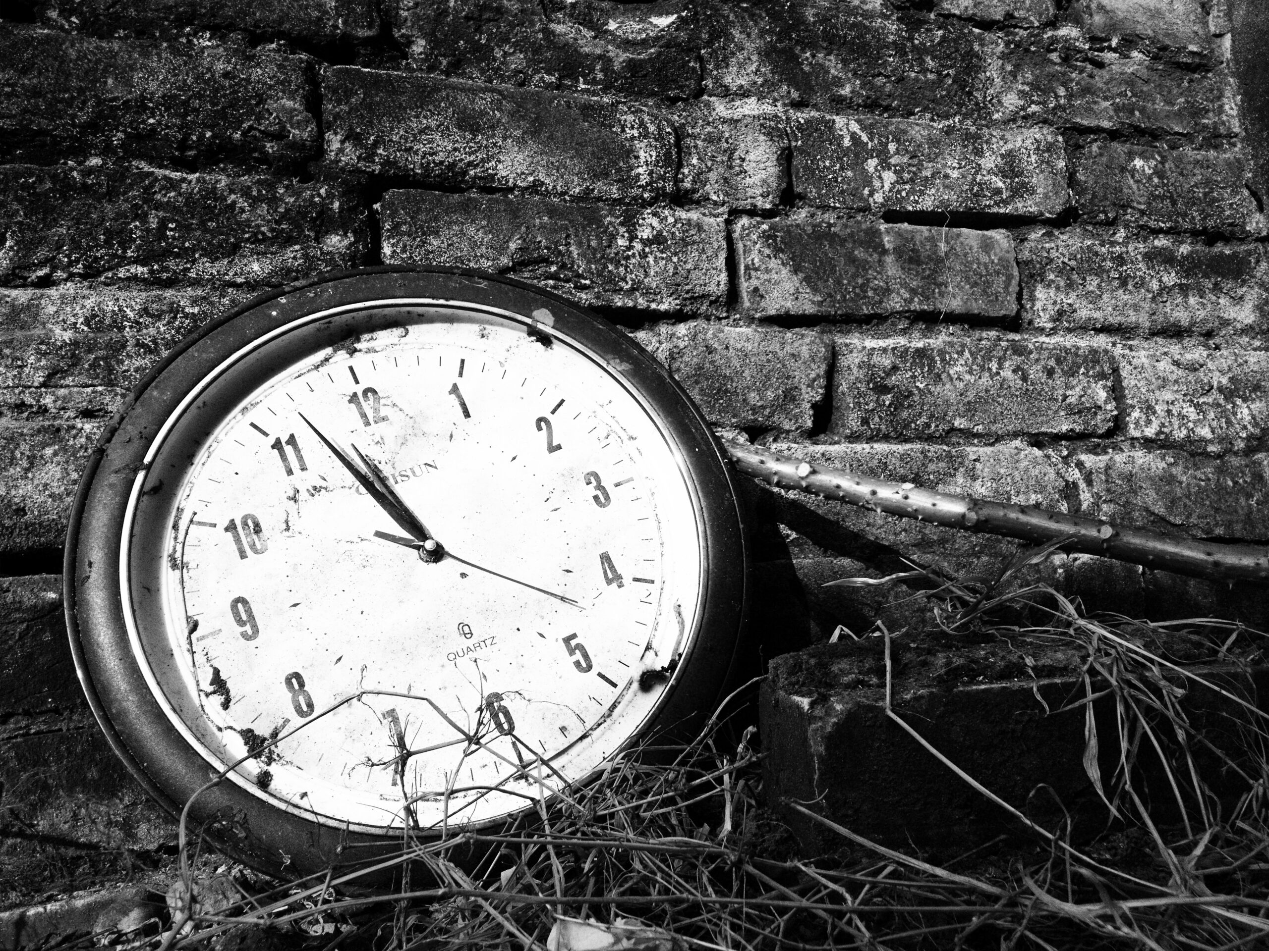 An analog clock sitting against a brick wall, with a grey scale filter
